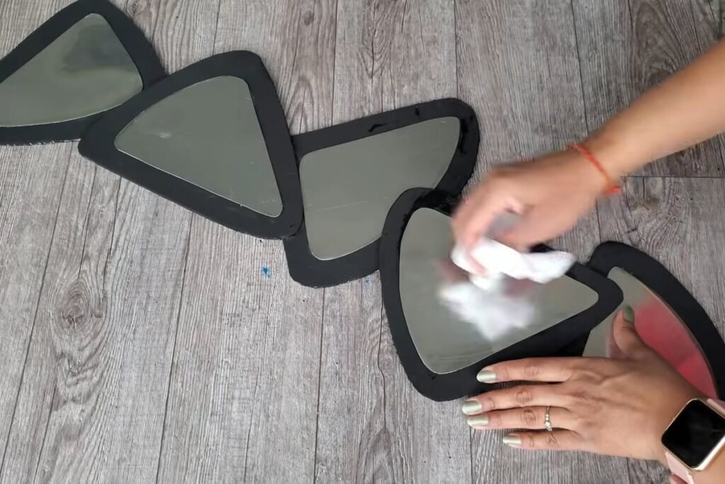 A hand wiping a rounded triangle mirror piece with a cloth while the other frames are already filled
