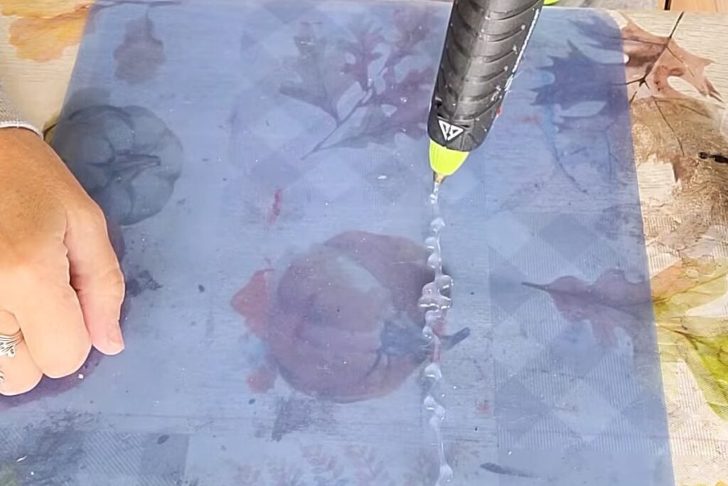 A hot glue gun drawing a zigzag line of clear glue on a smooth blue mat